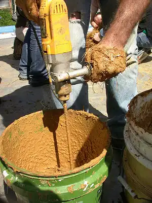 Mixing clay found on-site for the clay-slip-straw using a power drill with a paint mixing paddle